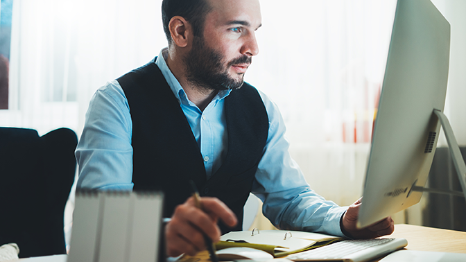 Engineering Man Sitting at Computer with Pen and Book